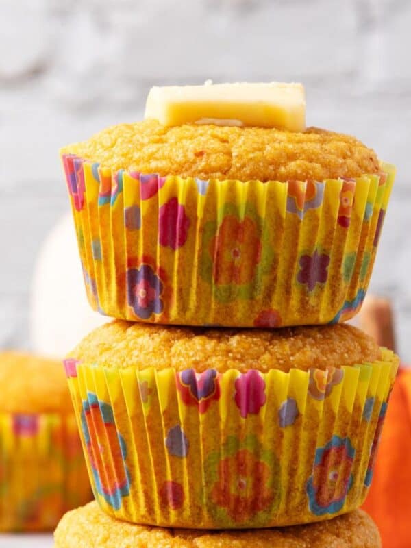 Pumpkin cornbread muffins stacked on top of each other with a pat of butter on top.