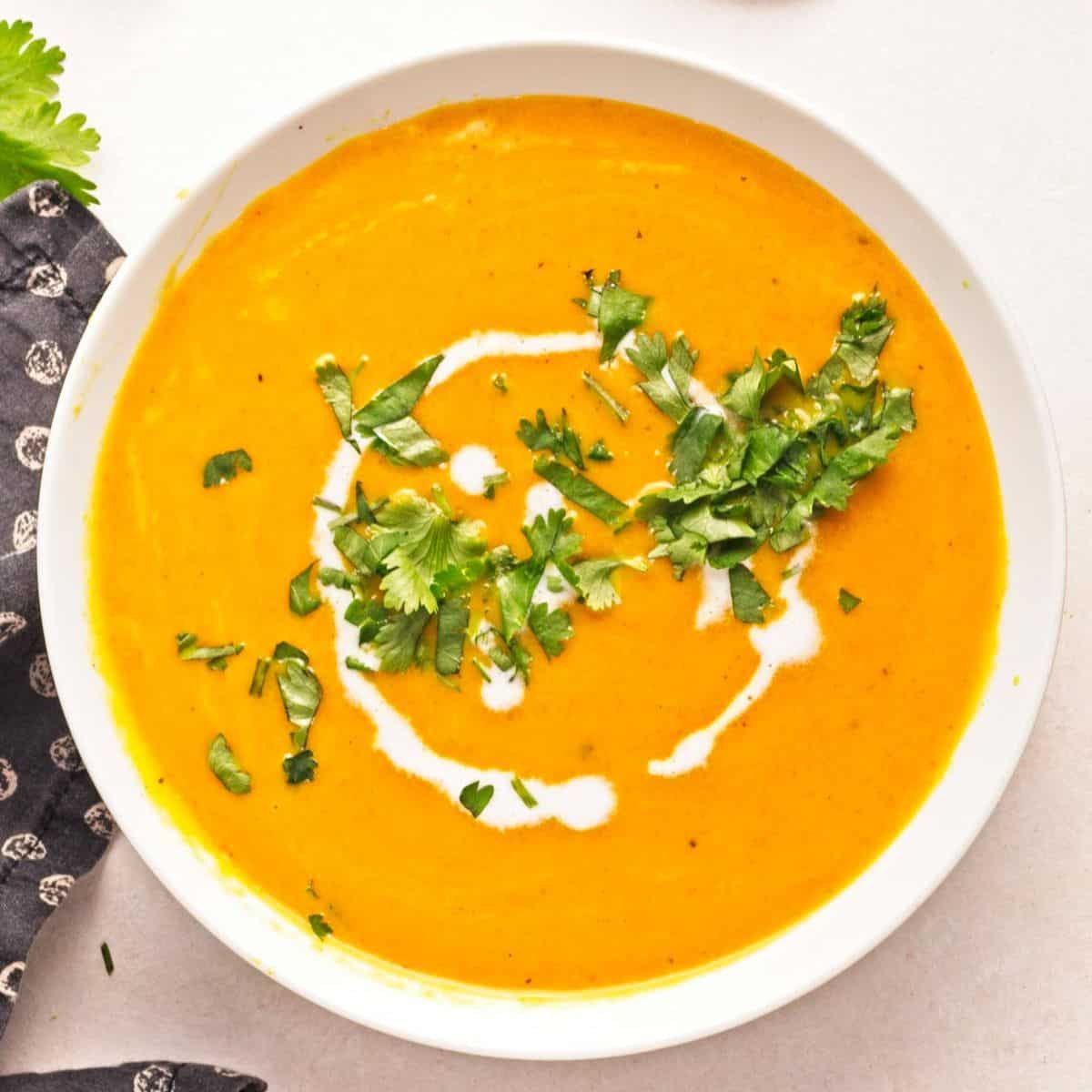 A bowl of curried carrot soup with coconut milk garnished with chopped cilantro and swirls of milk.