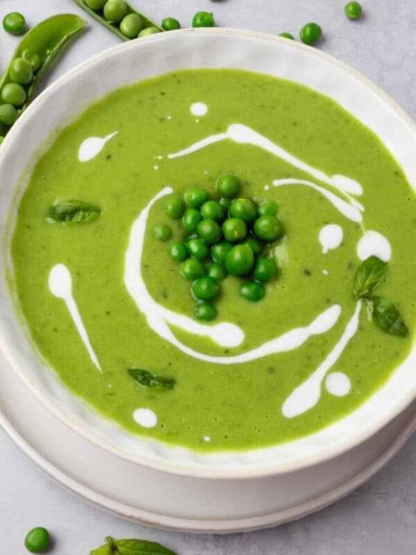 Green pea soup in a bowl garnished with peas, yogurt drizzle, and fresh basil.