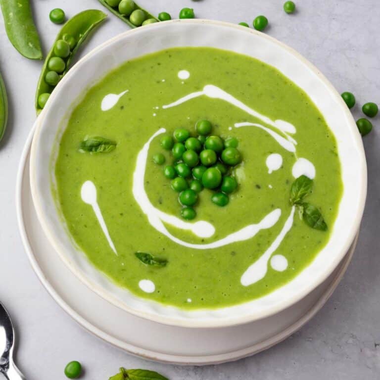 Green pea soup in a bowl garnished with peas, yogurt drizzle, and fresh basil.