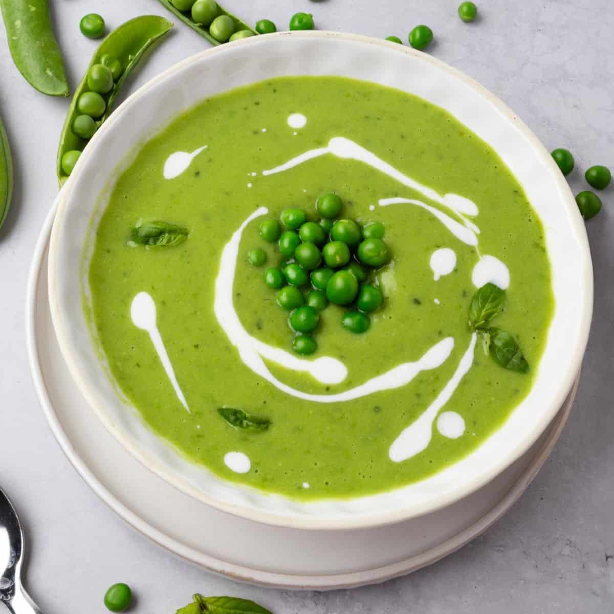 Green pea soup in a bowl garnished with peas, yogurt drizzle, and fresh basil.