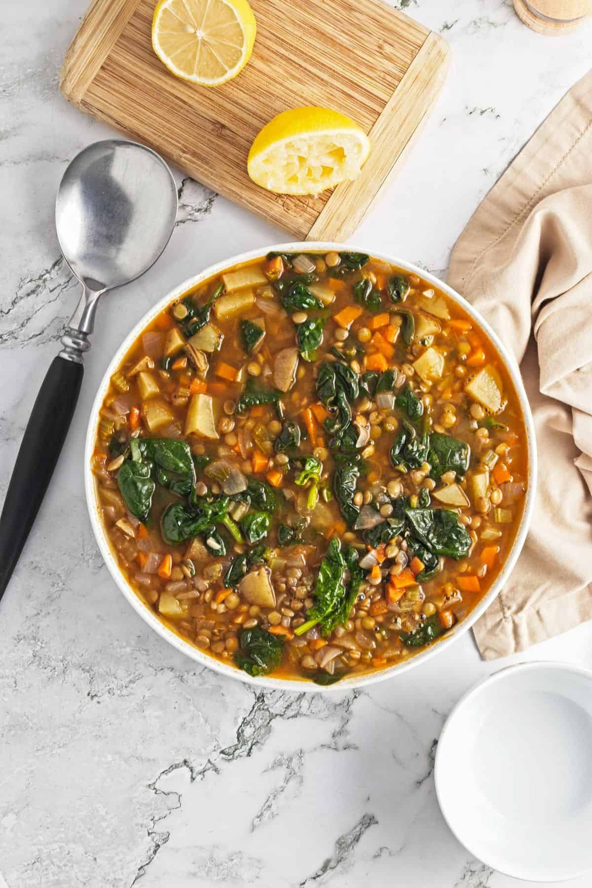 A bowl of spinach lentil soup on the table with a spoon and squeezed lemon to the side.