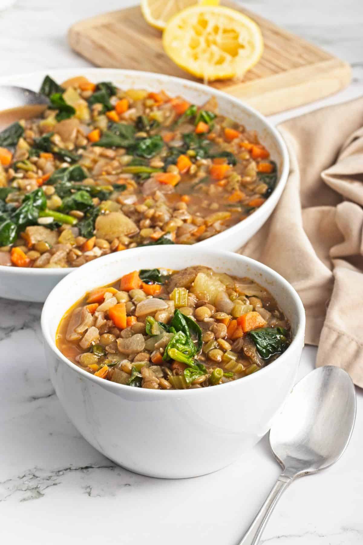 Two bowls of spinach and lentil soup on the table with a tan napkin to the side.