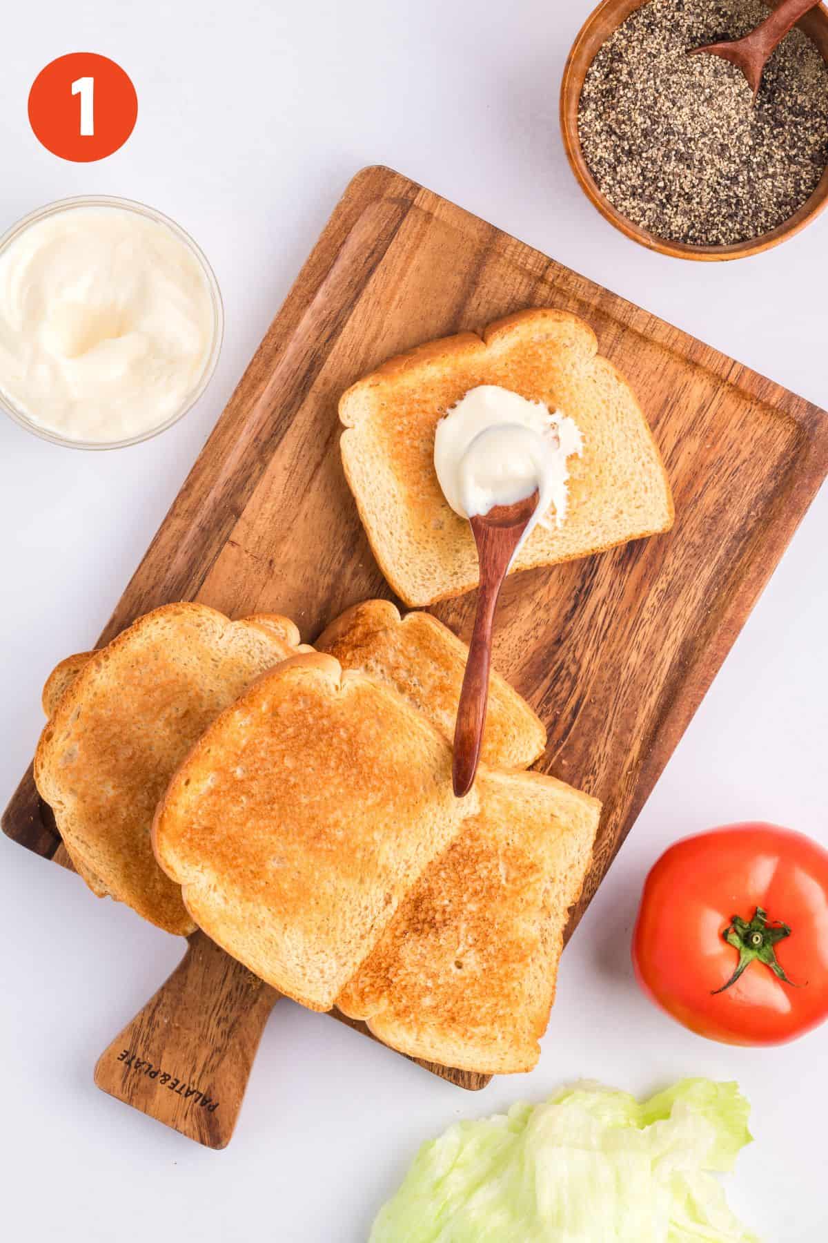 A spoon spreading mayo on a piece of toasted bread.