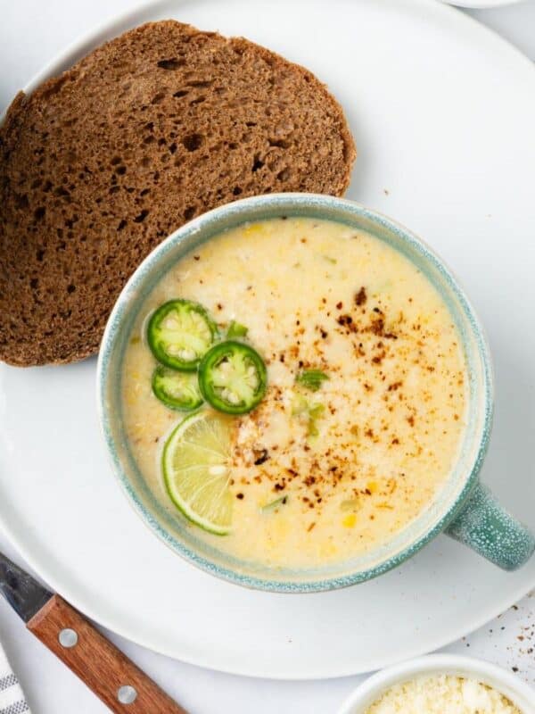 A blue cup of Mexican street corn soup on a white plate.