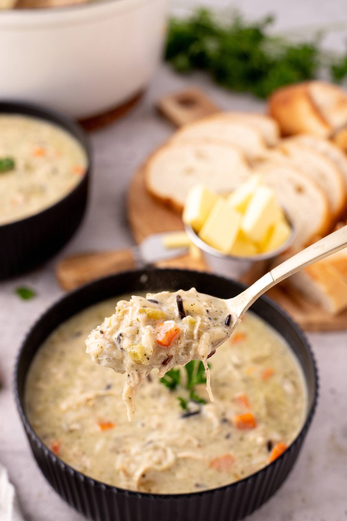 A spoonful of creamy chicken soup held up over the bowl.
