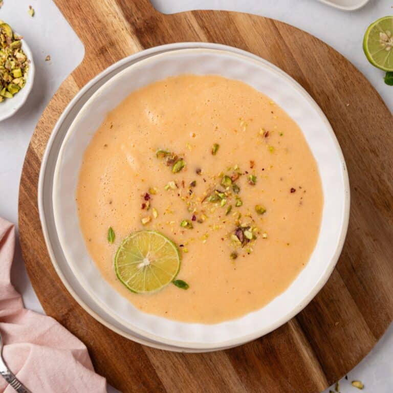 A bowl of melon soup on a round wooden cutting board.