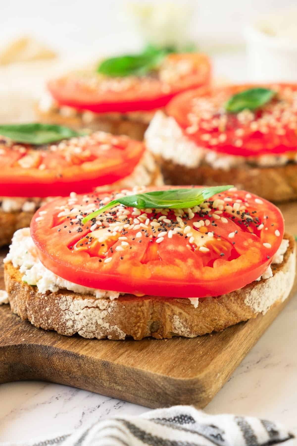 Ricotta toasts laid out on a wooden cutting board topped wtih tomato and fresh basil.