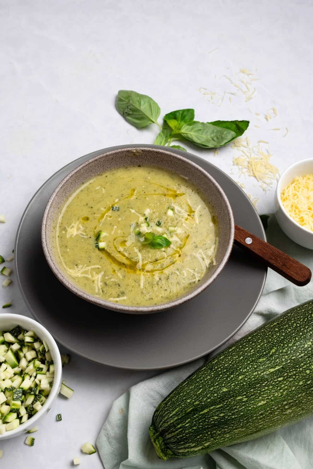 A bowl of zucchini basil soup garnished with a drizzle of olive and some diced zucchini.