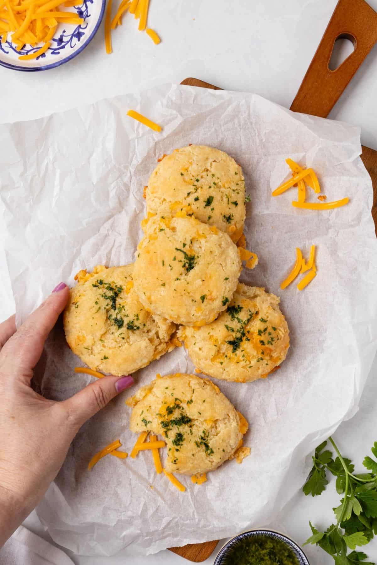 Cheese biscuits piled up on a piece of parchment paper on a cutting board.