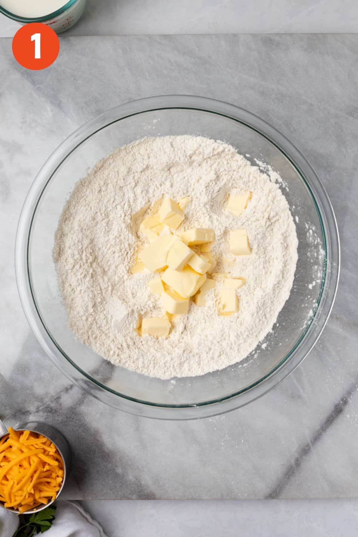 Butter added to dry ingredients in a glass mixing bowl.