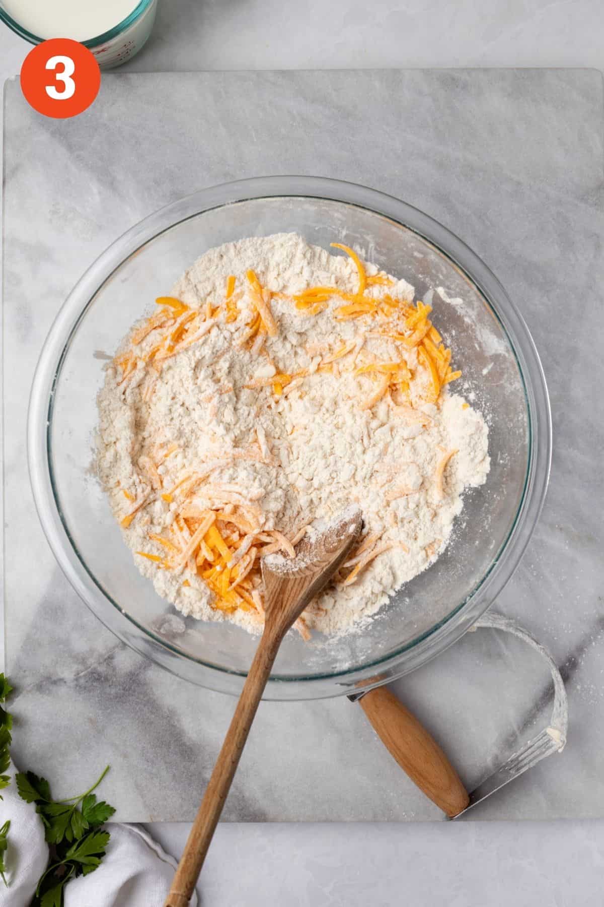 Adding cheddar cheese to the bowl with a wooden spoon.