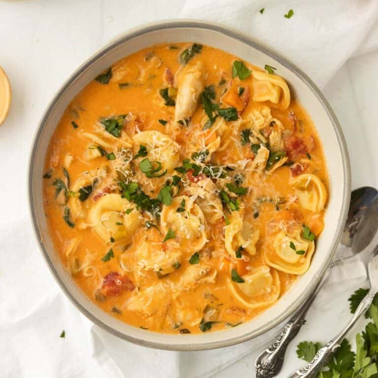 A bowl of creamy chicken tortellini soup with a spoon to the side.