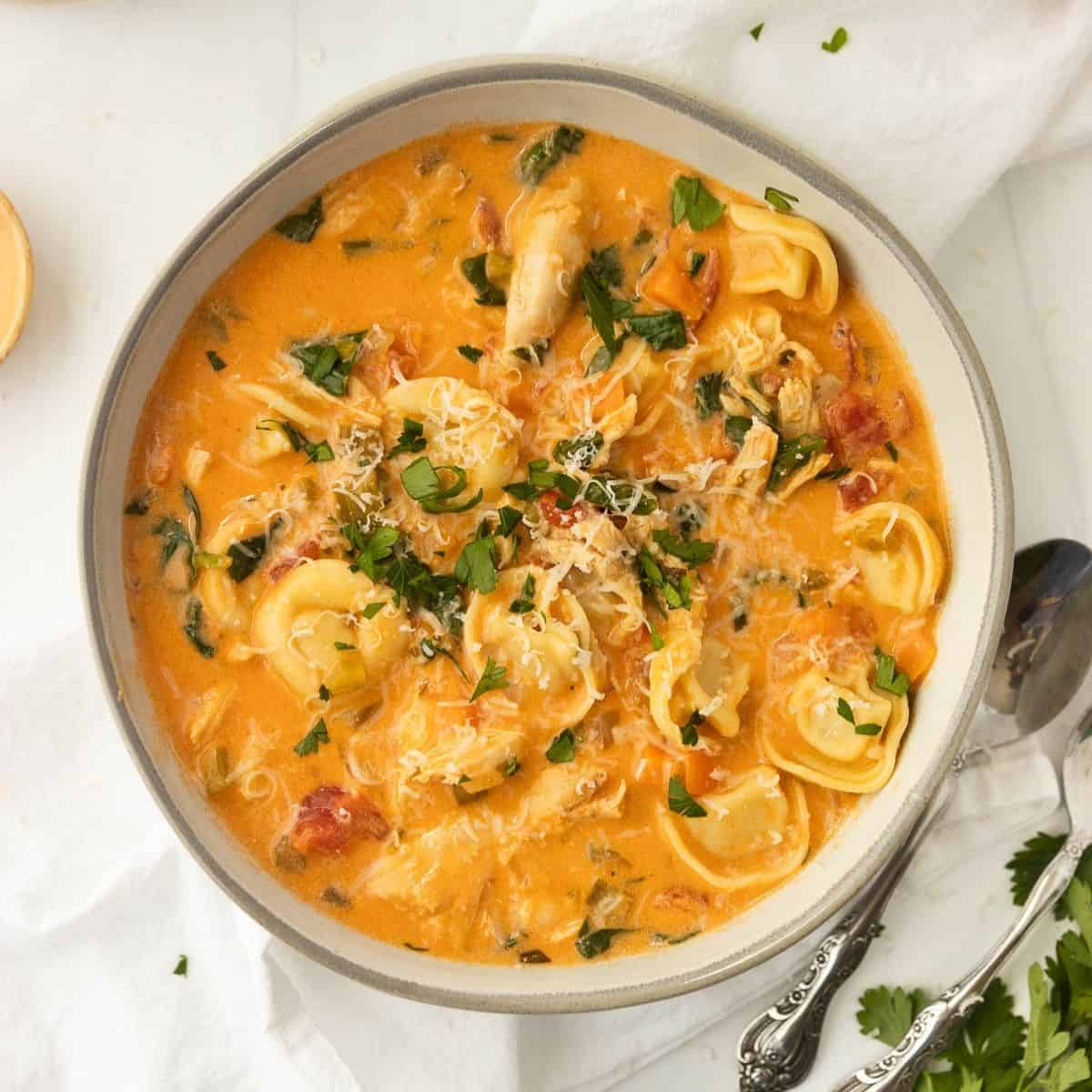 A bowl of creamy chicken tortellini soup with a spoon to the side.