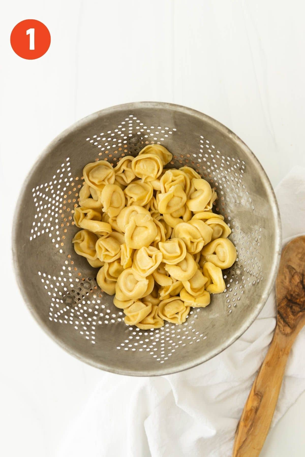 Cooked tortellini in a metal strainer.