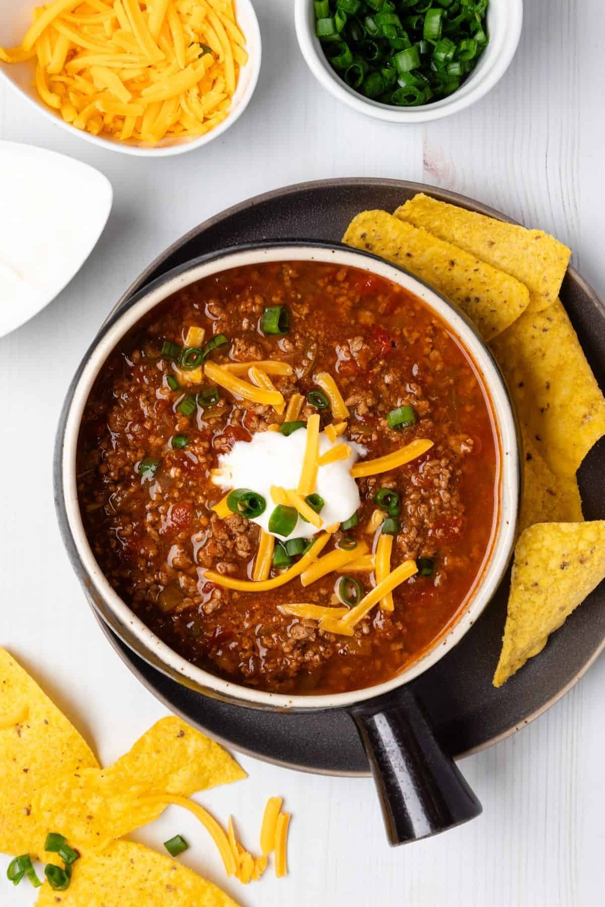 A bowl of no bean chili with bowls of sour cream, cheese, and green onions to the side.