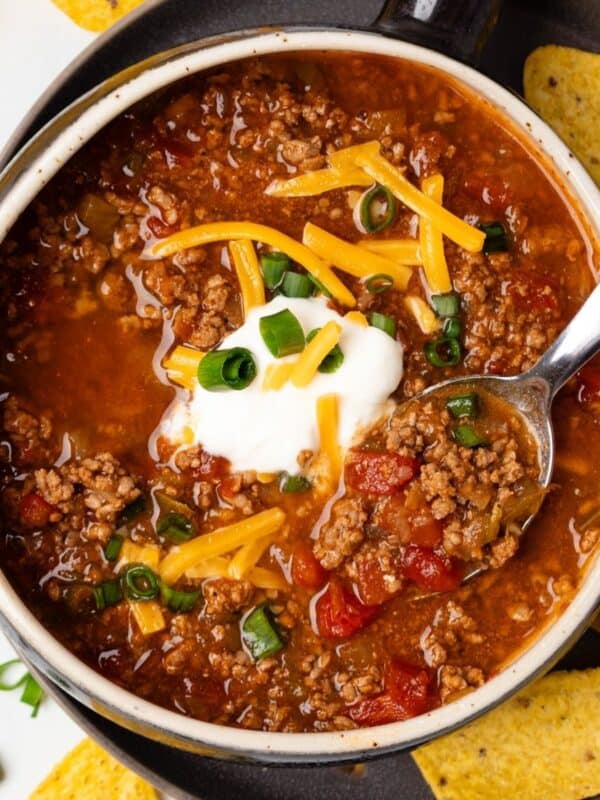 A bowl of no bean chili topped with sour cream and grated cheese with a spoon resting in the bowl.