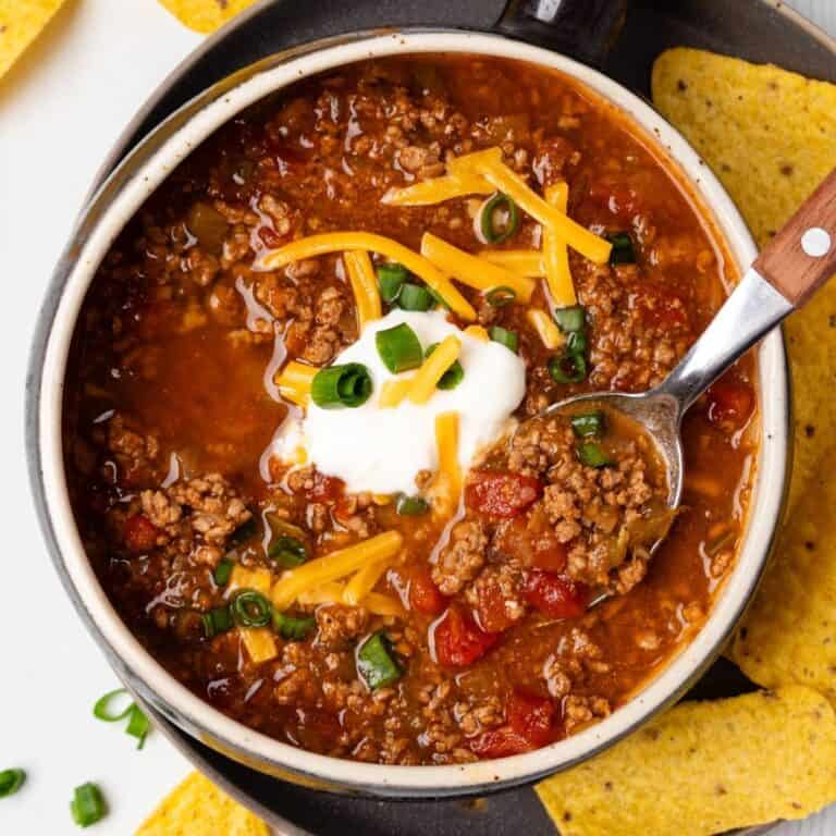 A bowl of no bean chili topped with sour cream and grated cheese with a spoon resting in the bowl.