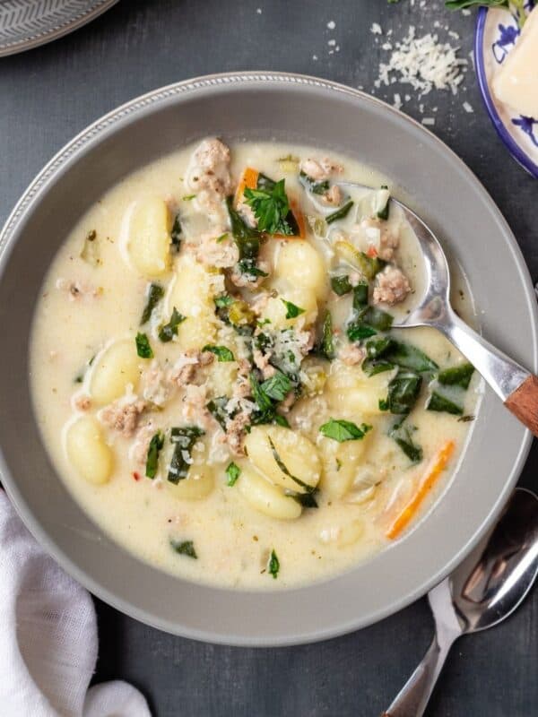 A bowl of sausage gnocchi soup with a spoon resting in the bowl.
