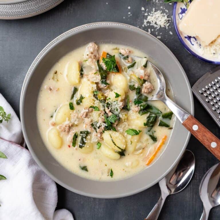 A bowl of sausage gnocchi soup with a spoon resting in the bowl.