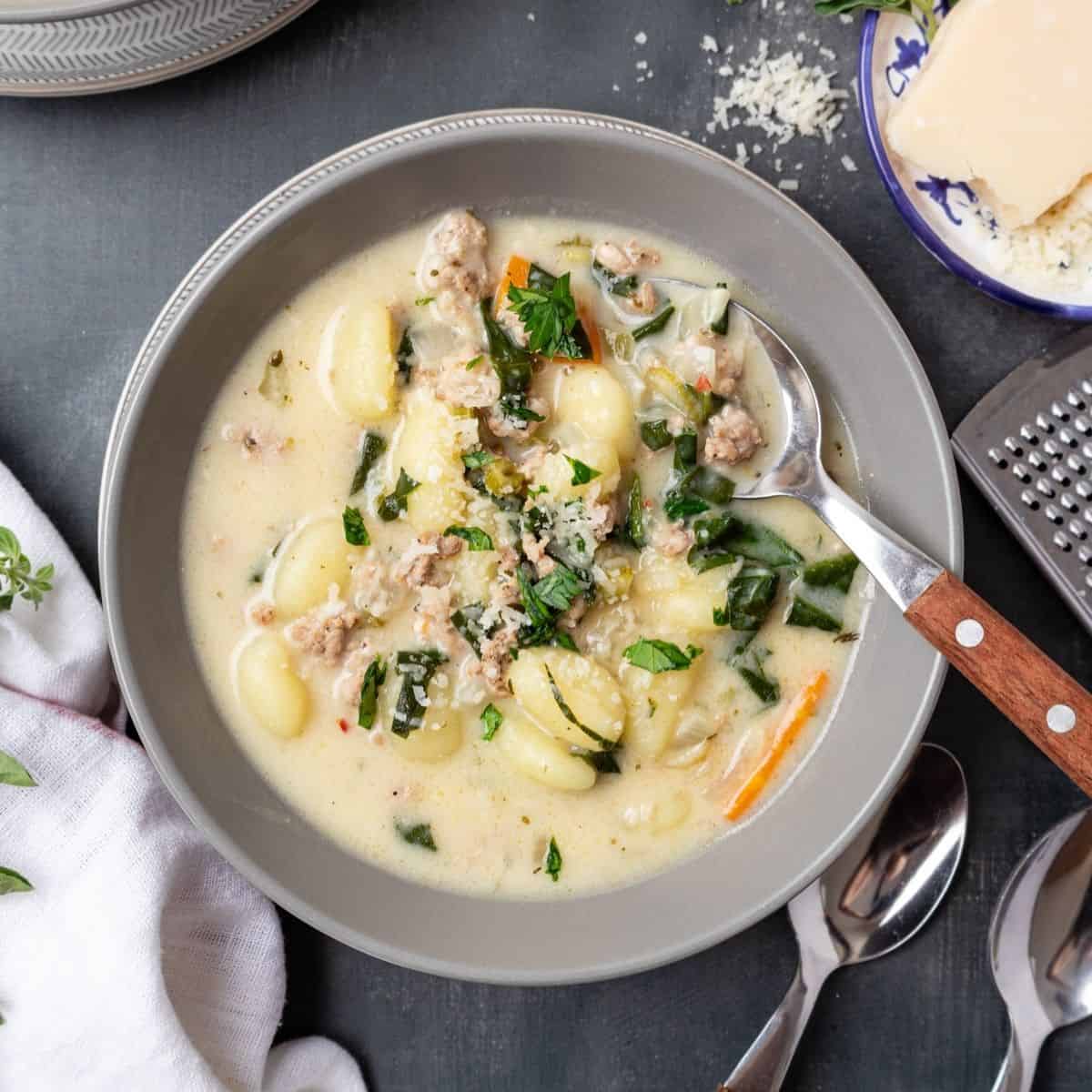 A bowl of sausage gnocchi soup with a spoon resting in the bowl.