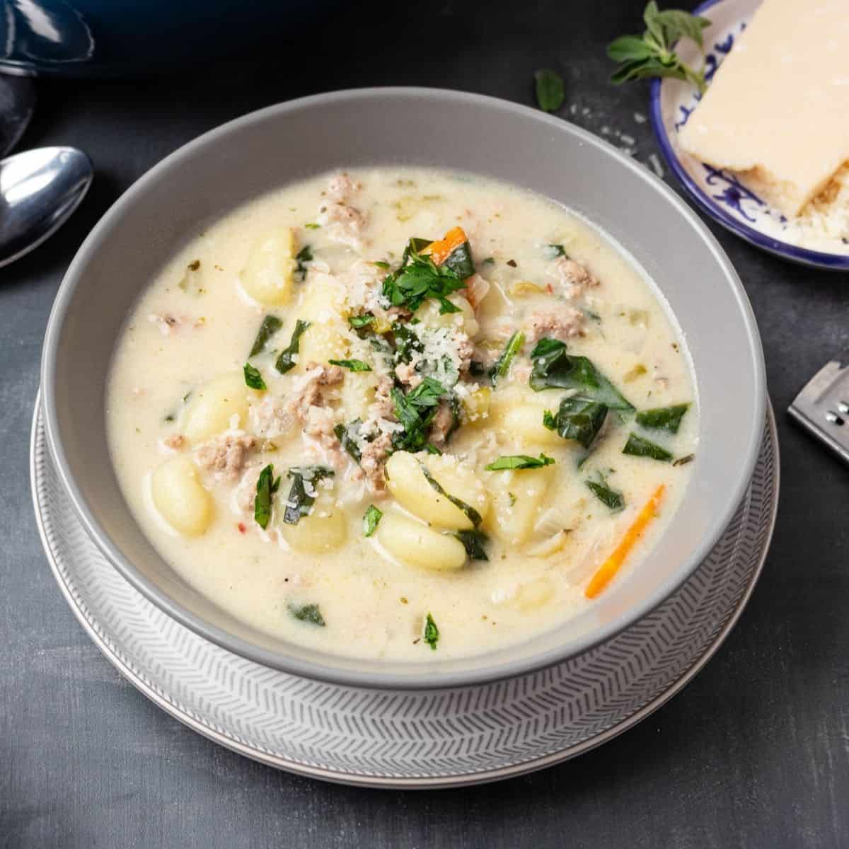 A bowl of sausage gnocchi soup on a plate.