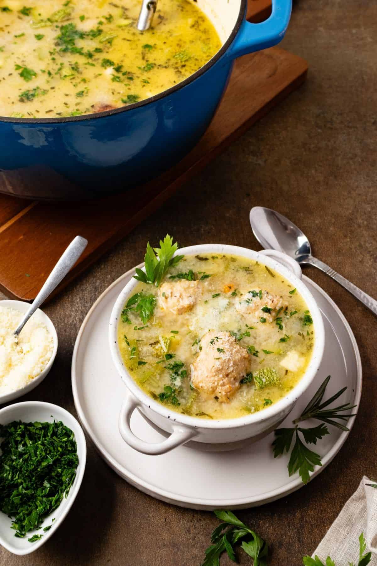 A bowl of chicken meatball soup in front of a pot of more.