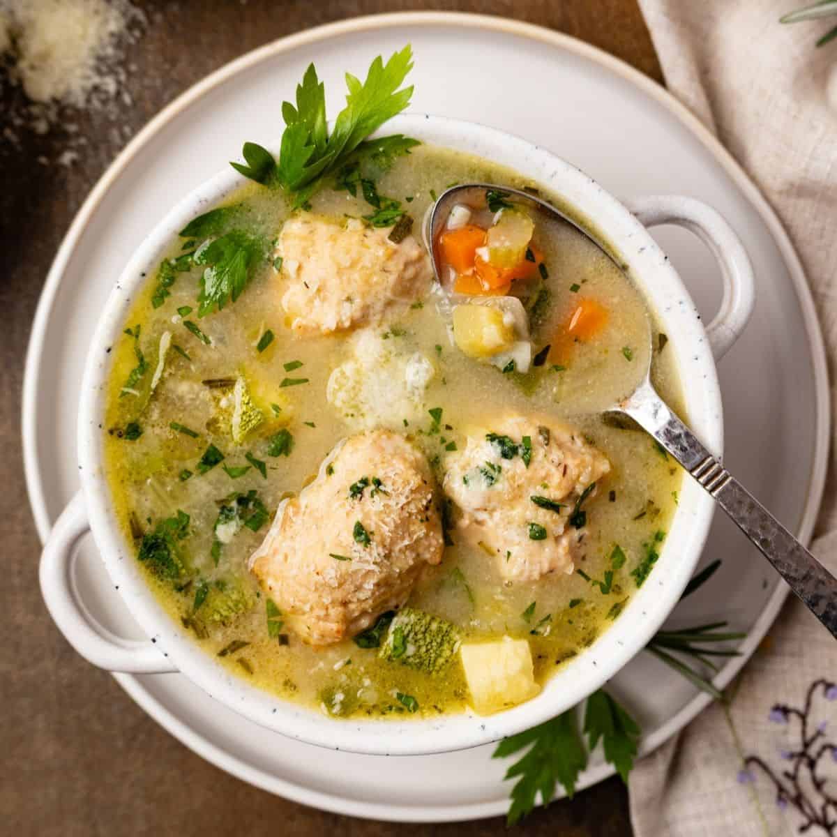 Chicken meatball soup with vegetables and a spoon resting in the soup.