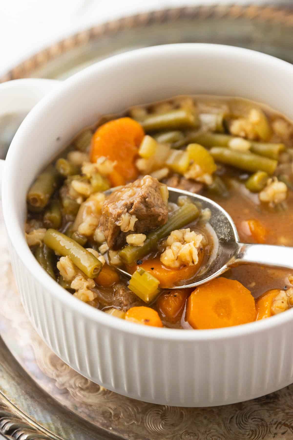 A spoon lifting up a bit of beef and barley soup from a bowl.