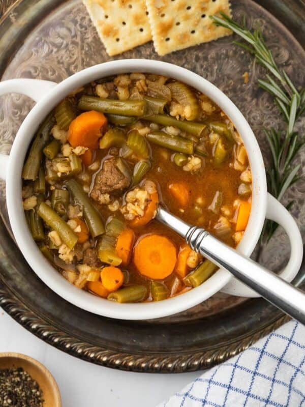 Instant pot beef barley soup in a white bowl on a silver platter with crackers to the side.