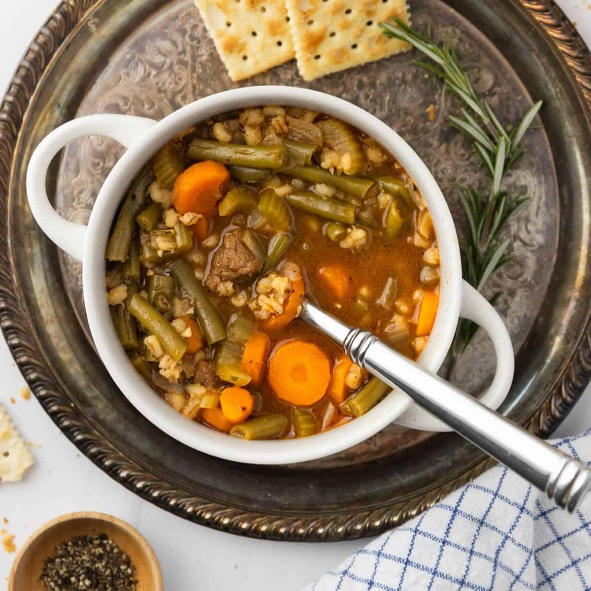Instant pot beef barley soup in a white bowl on a silver platter with crackers to the side.