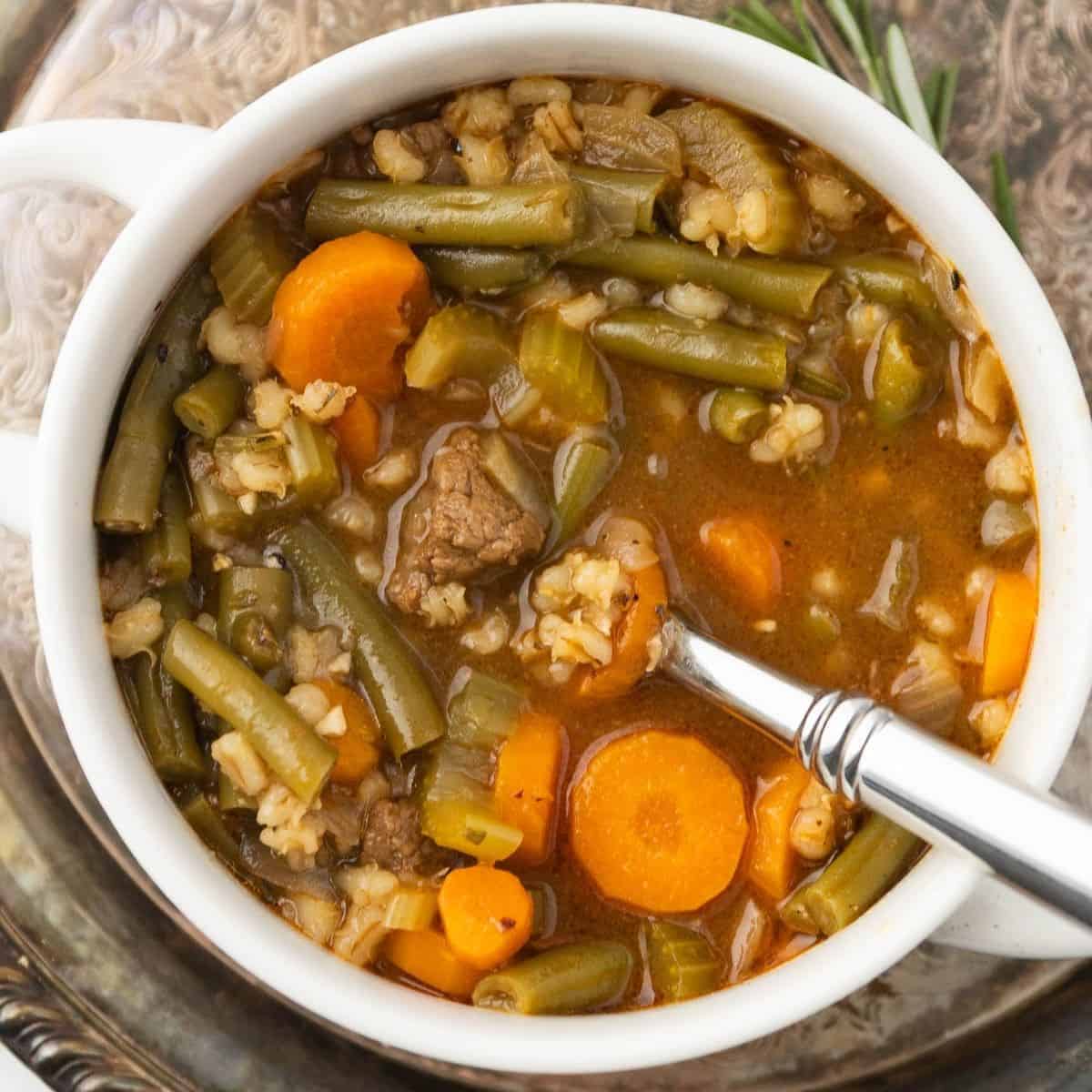 Beef barley soup in a white bowl with a spoon resting to the side.