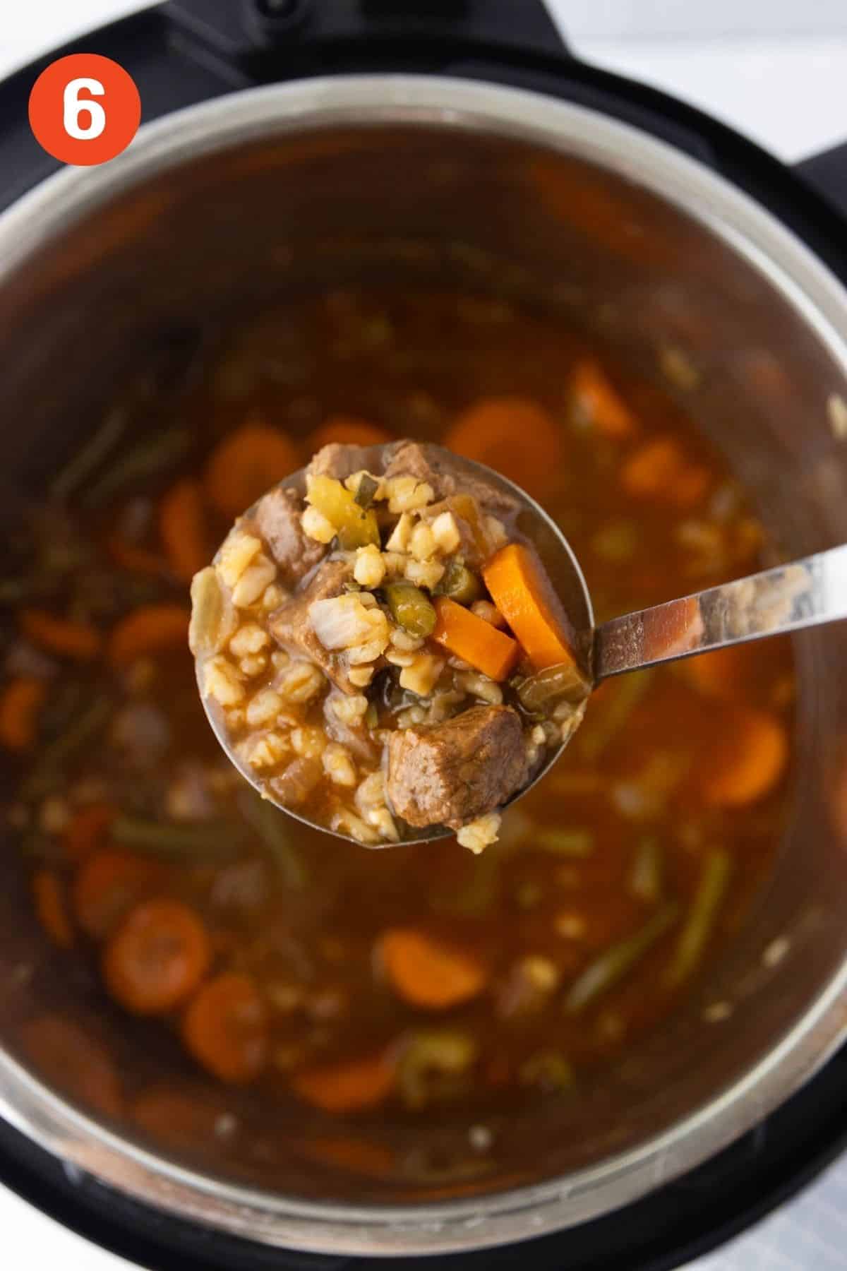 A ladle lifting up a serving of beef barley soup from the pot.