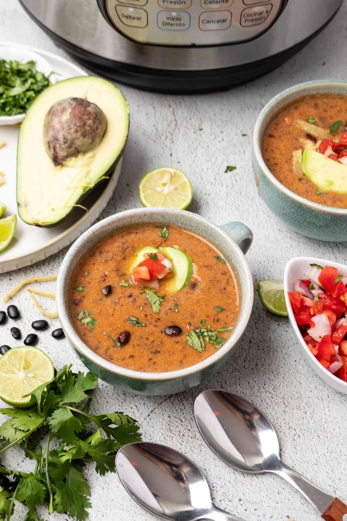 Bowls of black bean soup on a table with an Instant Pot in the background.