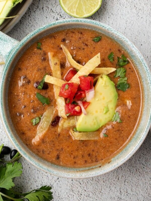 Instant pot black bean soup served in a blue soup cup garnished with tortillas and avocado.