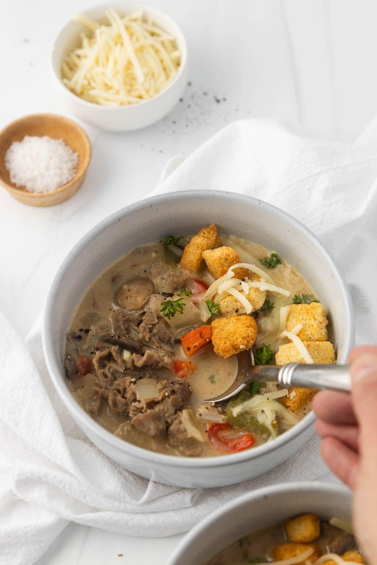 A bowl of philly cheesesteak soup with a spoon in the bowl.