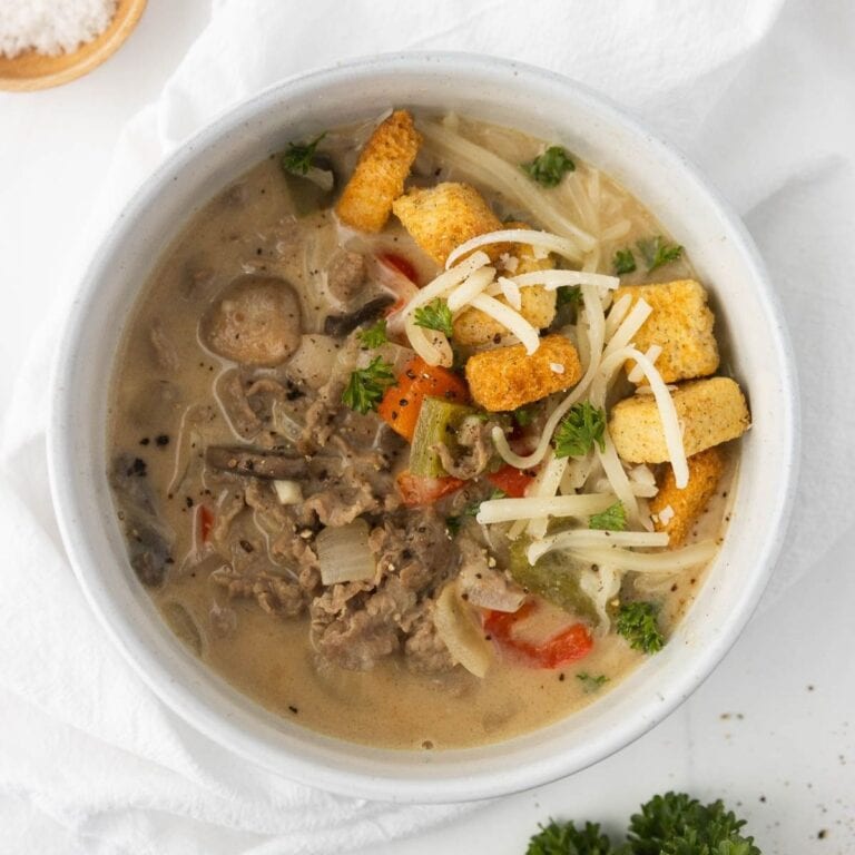 A bowl of Philly cheesesteak soup with shredded cheese and croutons on top.