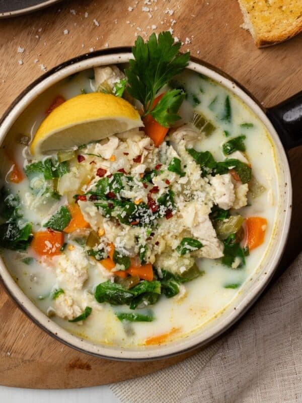 Chicken pastina soup served up in a bowl garnished with lemon wedge and a leaf of parsley.