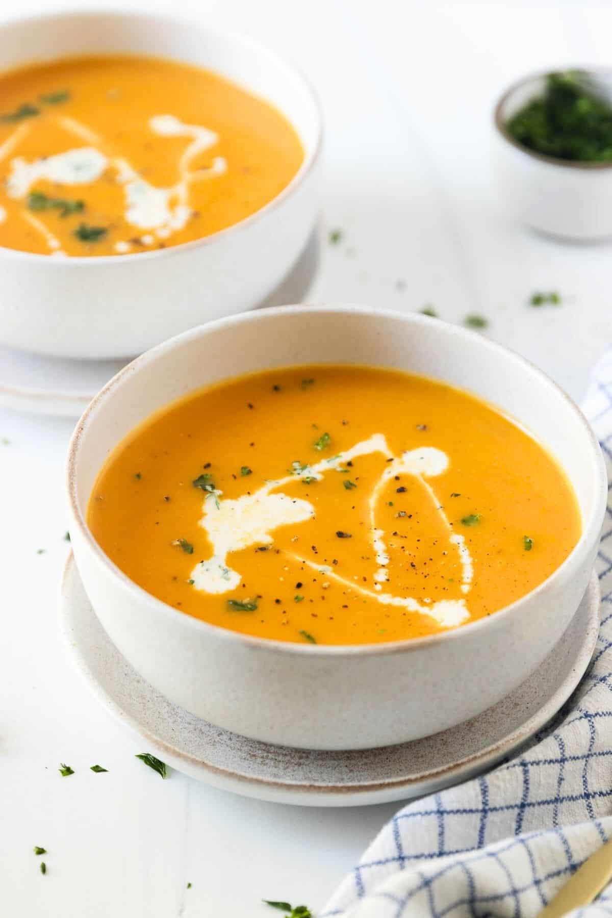 Bowls of Instant Pot butternut squash soup on a table with a bowl of parsley to the side. 