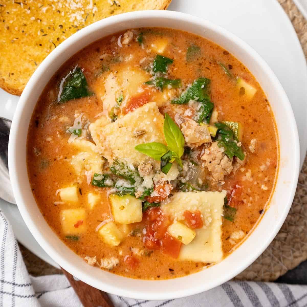 A bowl of ravioli soup garnished with fresh basil.