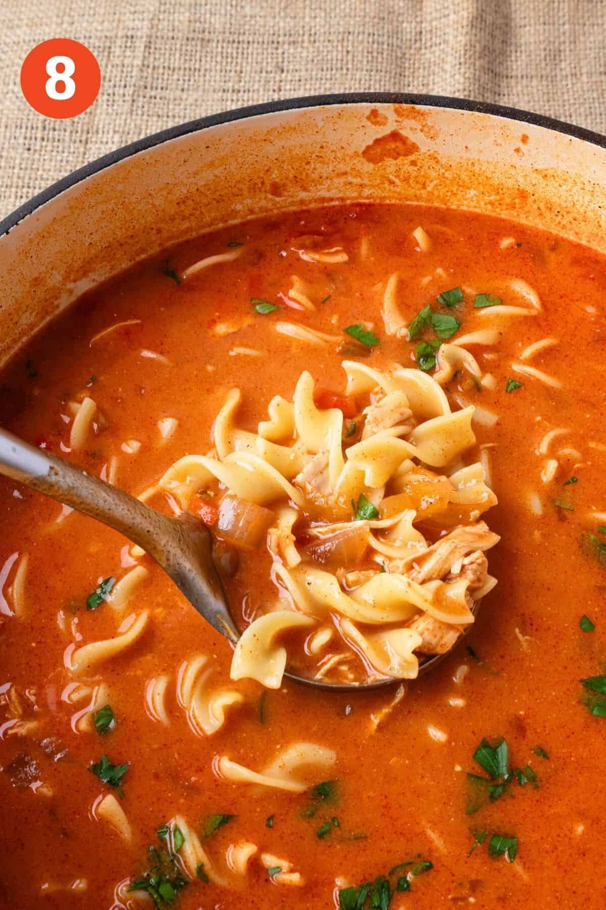 A ladle lifting a serving of chicken paprikash soup from the pot.
