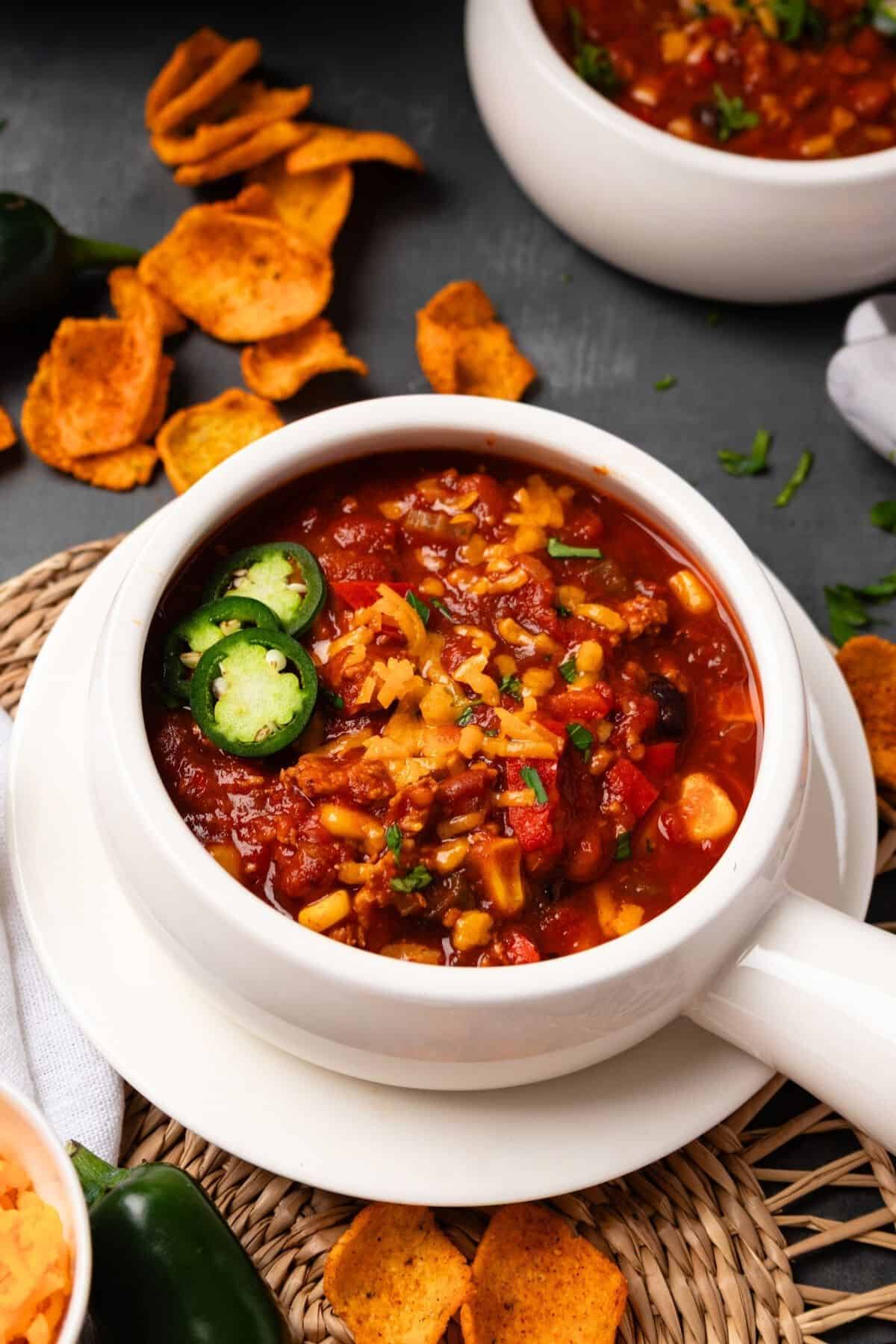 A white crock filled with Instant Pot turkey chili garnished with cheese and jalapenos.
