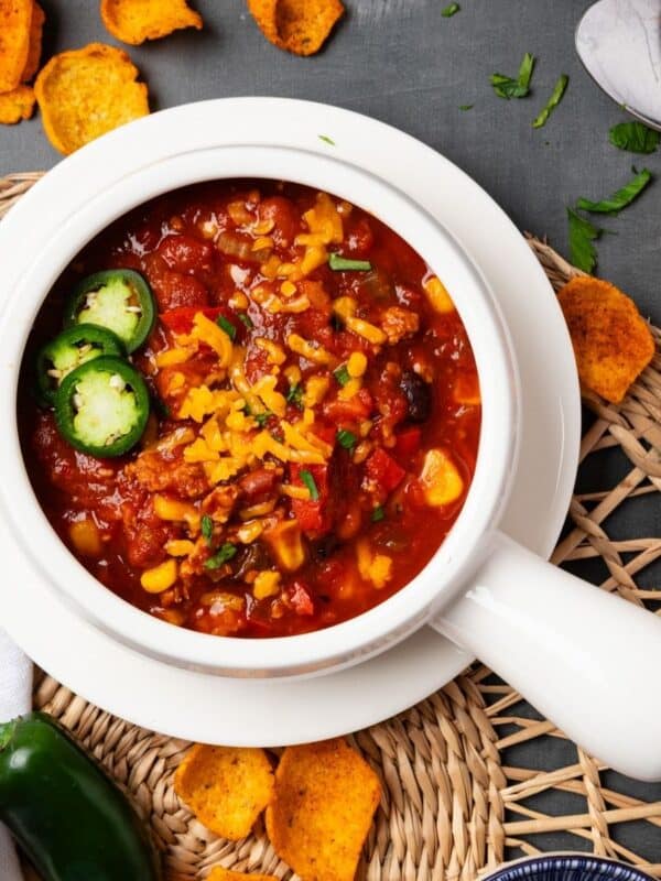 A white bowl of Instant pot turkey chili on a table with corn chips scattered around it.