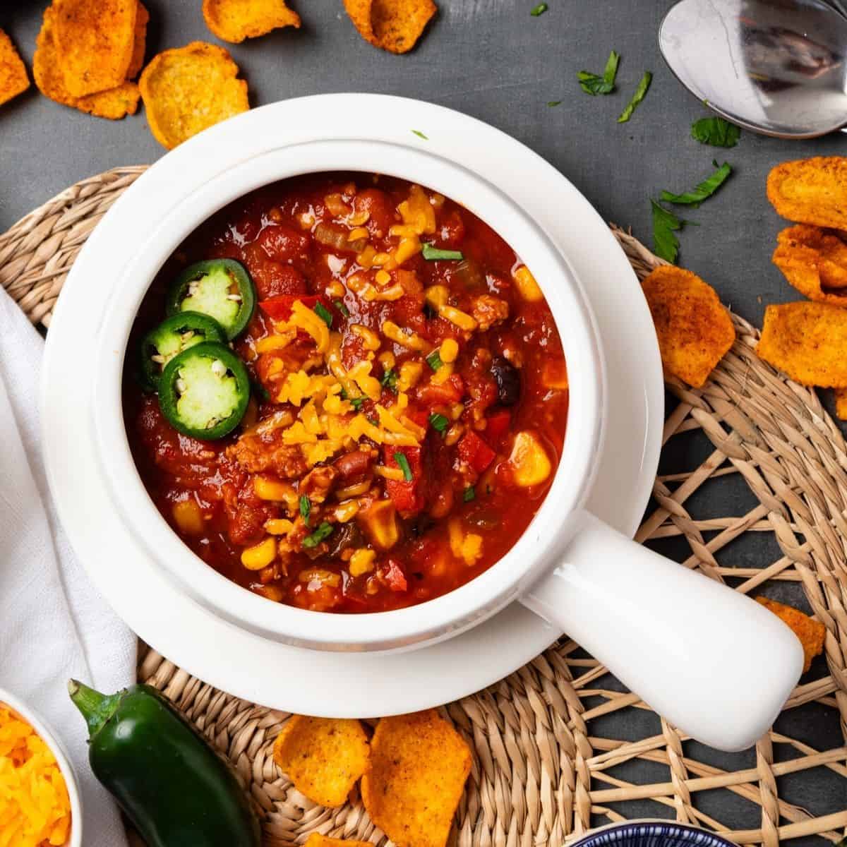 A white bowl of Instant pot turkey chili on a table with corn chips scattered around it.