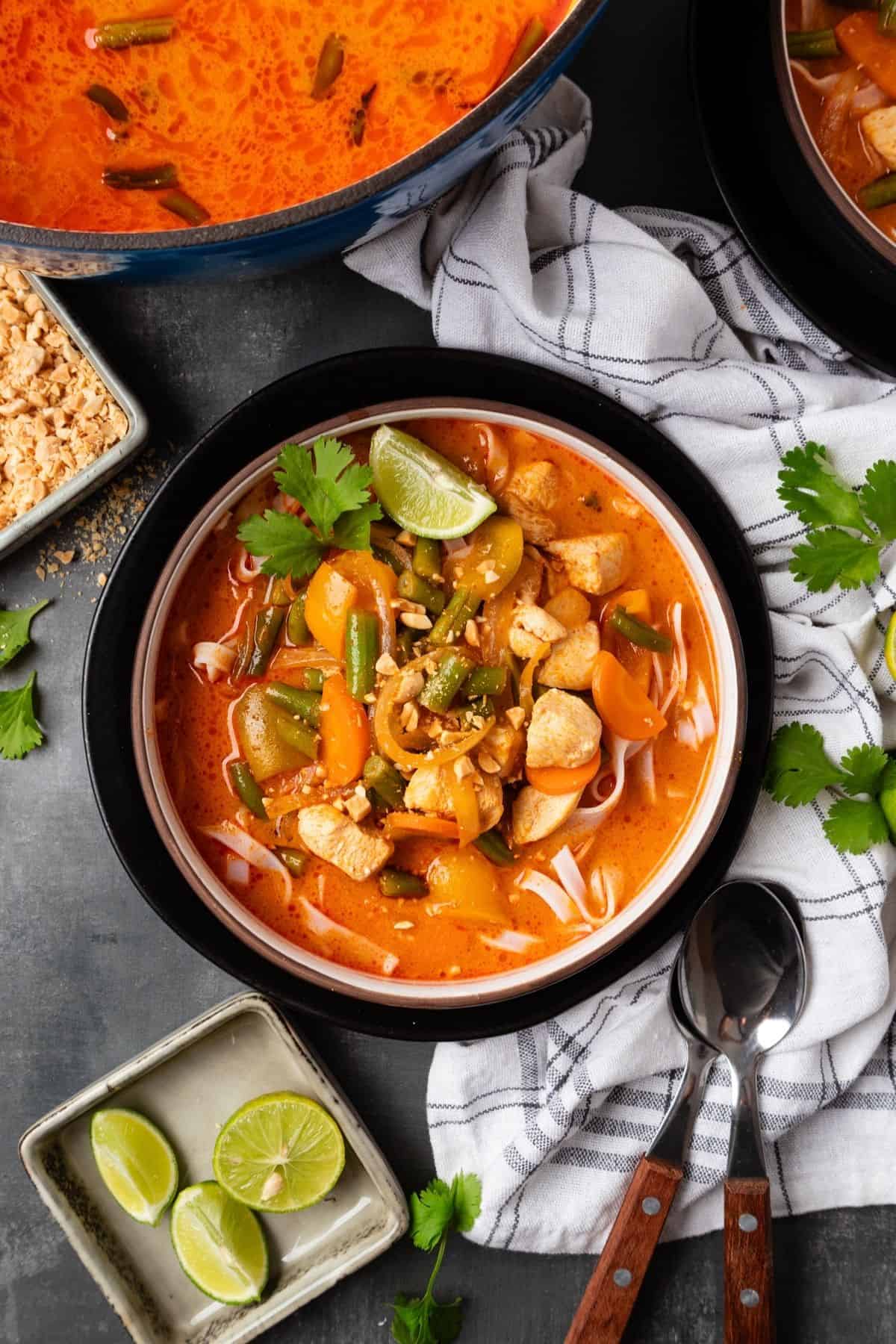 A bowl of Thai red curry soup with the pot of more in the corner.