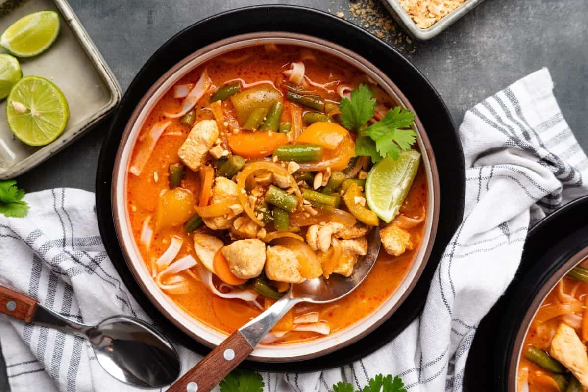 A bowl of Thai red curry soup on a table with a spoon resting in the bowl. 
