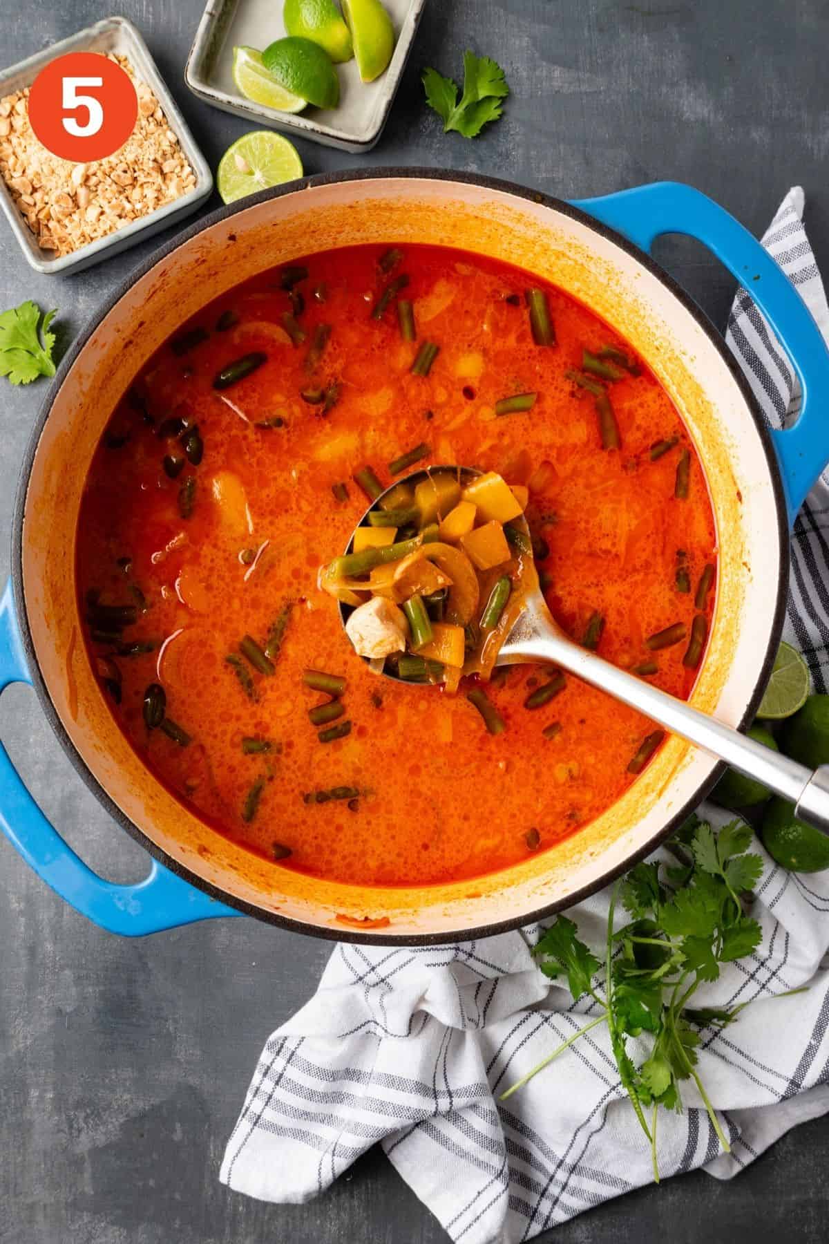 A pot of Thai curry chicken soup with a ladle lifting up a spoonful.
