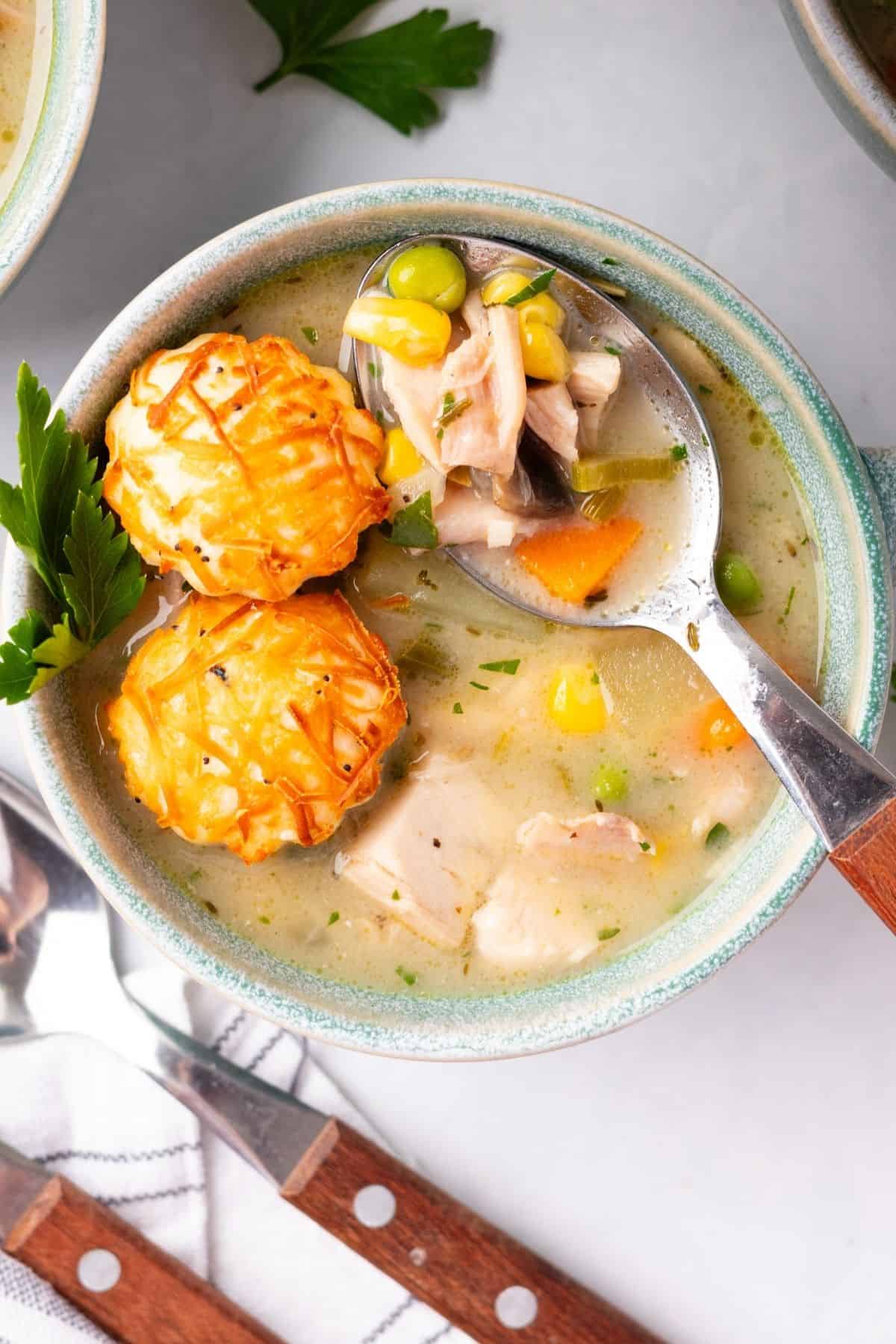 A spoon lifting up a bite of chicken pot pie soup in a bowl.