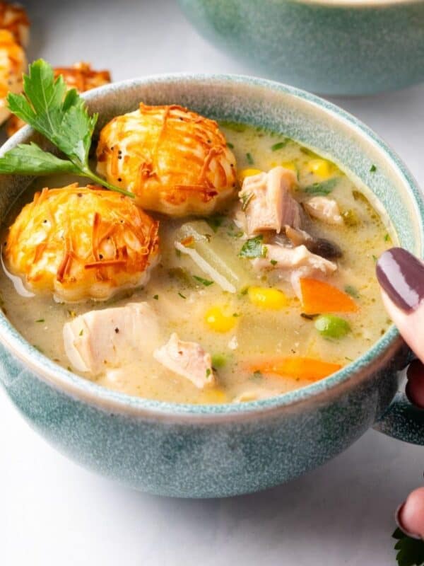 A blue cup of chicken pot pie soup with a hand holding it.