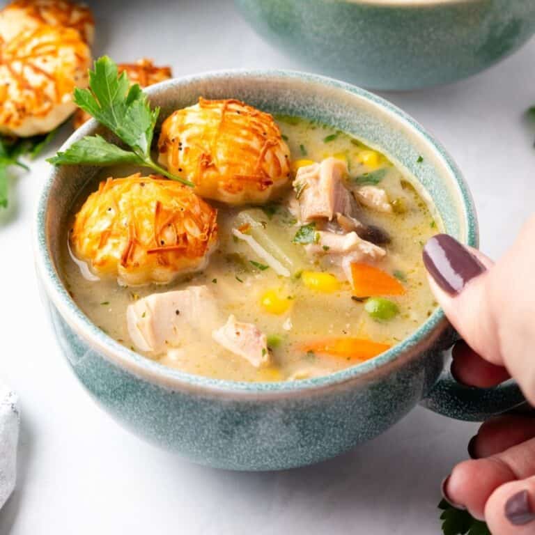 A blue cup of chicken pot pie soup with a hand holding it.